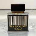 Paris Corner Autograph 100ml — A clear glass perfume bottle with a black label featuring a barcode and gold text "BARCODE Autograph" sits on a reflective surface with water droplets and splashes around it. | Paris Corner Autograph 100ml — Botol minyak wangi kaca jernih dengan label hitam menampilkan kod bar dan teks