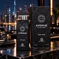 Grandeur Avenue New York EDP Lelaki — Botol dan kotak corak marmar hitam dengan aksen emas, berlatar belakang langit bandar yang kabur pada waktu malam. Jam tangan dan buku nota kelihatan.