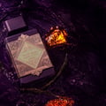 Lattafa Bade'e Al Oud Amethyst Fusion 100ml — A dark purple perfume bottle with a gold and green label, submerged in dark purple water with amber-like rocks and dried plant stems.
