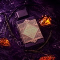 Lattafa Bade'e Al Oud Amethyst Fusion 100ml — A dark purple perfume bottle with a gold geometric label, submerged in dark purple liquid with amber-colored crystals and dark strands.