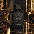 Lattafa Bade'e Al Oud Black Exposed — Black faceted perfume bottle with gold accents, set against dark, textured rocks and a blurred golden lantern.