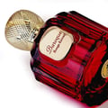Maison Alhambra Baroque Rouge Extrait 100ml by Maison Alhambra — Close-up of a red and black marbled glass perfume bottle with a textured gold cap, angled on a white background. | Maison Alhambra Baroque Rouge Extrait 100ml by Maison Alhambra — Pandangan dekat botol minyak wangi kaca berjalinan merah dan hitam dengan