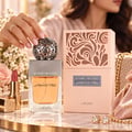 Lattafa Beyond Precious by Lattafa 100ml EDP Women — Tangan wanita bertakavih berlian meletakkan penutup perak berukir pada botol minyak wangi kaca jernih berisi cecair keemasan. Gincu merah jambu dan kotak hiasan turut kelihatan.