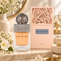 Lattafa Beyond Precious by Lattafa 100ml EDP Women — Botol minyak wangi kaca jernih berisi cecair oren dan penutup perak berhias, diletakkan bersebelahan kotak berwarna pic senada dengan ukiran menarik. Kain merah jambu lembut dan bunga putih mengelilingi paparan.