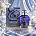 Lattafa Blue Oud Elixir — A blue glass perfume bottle with ornate silver accents and a silver-embossed box, displayed on a marble stand with silk drapes and white flowers.