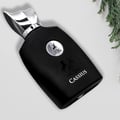 Maison Alhambra Cassius 100ml by Maison Alhambra — Black perfume bottle with silver cap and embossed horse emblem, angled on a white surface with green foliage on the right. | Maison Alhambra Cassius 100ml by Maison Alhambra — Botol minyak wangi hitam dengan penutup perak dan lambang kuda timbul, condong di permukaan