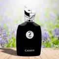 Maison Alhambra Cassius 100ml by Maison Alhambra — A black perfume bottle with a silver, animal-shaped cap and a circular logo featuring a deer, set against a blurred background of purple flowers and greenery. | Maison Alhambra Cassius 100ml by Maison Alhambra — Botol minyak wangi hitam dengan penutup perak berbentuk