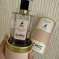 Maison Alhambra Chic Velvet Pink Secret for Women 100ml — A clear glass perfume bottle with a pink label featuring a deer logo and gold accents, resting in a pink cylindrical box with a gold rim. A matching pink cylindrical box is beside it. | Maison Alhambra Chic Velvet Pink Secret for Women 100ml — Botol minyak
