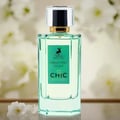 Maison Alhambra Chic Velvet Vert Secret 100ml — A clear glass perfume bottle with green liquid and a green label featuring a deer logo and text, set against a soft, blurred background of white flowers. | Maison Alhambra Chic Velvet Vert Secret 100ml — Botol kaca jernih berisi cecair hijau dan label hijau menampilkan
