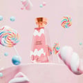 Khadlaj Cloud Candy Eau De Parfum — A pink perfume bottle with white cloud designs, surrounded by colorful lollipops, marshmallows, and blue spheres against a soft pink background. | Botol minyak wangi merah jambu dengan rekaan awan putih, dikelilingi oleh lolipop berwarna-warni, marshmallow, dan sfera biru