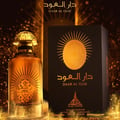 Paris Corner Daar Al Oud Intense 100ml — A golden sunburst design adorns a perfume bottle and its box, set against a dark, sparkling background. | Paris Corner Daar Al Oud Intense 100ml — Reka bentuk pancaran matahari keemasan menghiasi botol minyak wangi dan kotaknya, berlatarkan latar belakang gelap yang berkilauan.