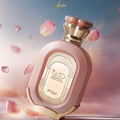 Zimaya Daiman Eden Eau De Parfum 100ml by Zimaya — A pink textured perfume bottle with gold accents and a gold label, surrounded by floating pink rose petals and golden sparkles against a soft blue and pink gradient background. | Zimaya Daiman Eden Eau De Parfum 100ml by Zimaya — Botol minyak wangi merah jambu