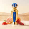 Bujairami Drip No. 7 Bujairami 100ml EDP — Gold and blue ornate perfume bottle with crown cap, surrounded by grapefruit slices and red currants on a sandy, misty background.