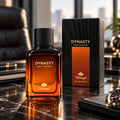 TADangel Dynasty by TADangel 100ml EDP Men — Botol minyak wangi kaca perang dengan penutup hitam, sebelah kotak hitam dan orennya, di atas meja marmar bersama buku nota kulit dan pen.