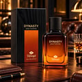 TADangel Dynasty oleh TADangel 100ml EDP Lelaki — Kotak hitam bertekstur dan botol minyak wangi kaca perang dengan penutup hitam, diletakkan di atas meja kayu bersama dompet kulit dan pen.