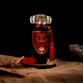 Lattafa Mohra by Lattafa 100ml EDP — Dark glass perfume bottle with a red ornate label featuring a tree design, topped with a faceted crystal cap and a red tassel, set on a wooden slice with cinnamon sticks and red roses.