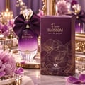 TADangel Fleur Blossom by TADAngel 100ml EDP Women — Purple gradient perfume bottle with a large satin bow and crystal stopper, next to its matching purple box with gold floral design, surrounded by pink flowers and petals on a marble surface.
