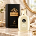 Maison Alhambra Galatea by Maison Alhambra 100ml EDP Unisex — Black box with gold accents and deer logo next to a pale gold perfume bottle with a gold cap, on a marble surface with silk fabric and flowers in the background.