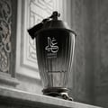 Zimaya Ghali Imperial Eau De Parfum 100ml by Zimaya — A black, fluted glass perfume bottle with a tasseled lid sits on a marble surface, with ornate architectural details in the background. | Zimaya Ghali Imperial Eau De Parfum 100ml by Zimaya — Botol kaca hitam berlekuk dengan penutup bertali duduk di atas permukaan
