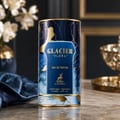 Maison Alhambra Glacier Flora 100ml — A tall, cylindrical perfume bottle with a dark blue and gold floral design, featuring the brand name and product details. It sits on a marble surface with a blue satin cloth and a vase of white flowers in the background. | Maison Alhambra Glacier Flora 100ml — Botol minyak wangi