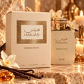 RASASI Hawas Addiction by Rasasi 100ml EDP — Kotak dan botol minyak wangi berwarna krim dengan perincian emas, berlatar belakang batu bertekstur, buah vanila, bunga putih, dan lilin menyala.