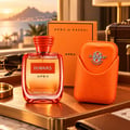 Kenz de Rasasi Hawas Apex — Botol minyak wangi oren dan sarung sepadan dengan logo timbul, diletakkan di atas dulang kulit dengan cermin mata hitam dan beg pakaian di latar belakang.