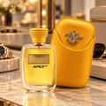 Kenz de Rasasi Hawas Apex GT — Yellow textured case with silver emblem next to a clear glass perfume bottle with gold cap and label, on a marble surface.