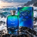 RASASI Hawas Atlantis by Rasasi 100ml EDP — Botol kaca gradien biru dan hijau dengan penutup bertekstur perak, diletakkan di atas batu gelap basah dengan ombak laut melanda di latar belakang.