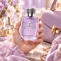 Kenz de Rasasi Hawas Desire For Her — Tangan wanita pegang botol minyak wangi kaca ungu dengan rekaan ular perak dan penutup perak, dengan latar belakang ungu lembut bersama beg tangan dan bunga.