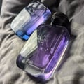 Rasasi Hawas For Him Eau De Parfum — Two glass perfume bottles with purple and blue gradients, one with a textured black cap, resting on a grey textured fabric surface. | Dua botol minyak wangi kaca dengan gradien ungu dan biru, satu dengan penutup hitam bertekstur, diletakkan di atas permukaan fabrik kelabu