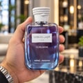 Kenz de Rasasi Hawas Ice Ultradose 100ml Lelaki — Tangan memegang botol minyak wangi kaca jernih berisi cecair ungu, bertutup tali putih dan label putih dengan tulisan Arab dan Inggeris.