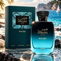 RASASI Hawas Malibu by Rasasi 100ml EDP — Teal box and gradient blue bottle with textured black cap, set on wet rocks with a beach and sailboat background.