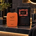 RASASI Hawas Overdose by Rasasi 100ml EDP — Orange perfume bottle and its black textured box with orange accents, displayed on a dark marble countertop with a plant and soap dispenser in the background.