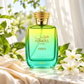 RASASI Hawas Verde by Rasasi 100ml EDP — Botol kaca gradien hijau dan kuning dengan penutup emas berhias, dikelilingi daun hijau dan bunga putih di atas permukaan marmar dengan fabrik.