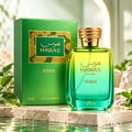 RASASI Hawas Verde by Rasasi 100ml EDP — Botol minyak wangi kaca gradien hijau dan kuning dengan penutup emas seperti ular, bersebelahan dengan kotak hijaunya, dipamerkan di atas permukaan batu bertekstur dengan pantulan air dan daun hijau.