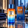 TADangel Intrigue Aquatic by TadAngel 100ml EDP Unisex — Botol minyak wangi gradien dari oren ke biru, bertudung biru, terletak di atas permukaan marmar basah bersebelahan kotak biru dan orennya. Tuala biru gelap berlipat dan dispenser sabun kelihatan di latar belakang.