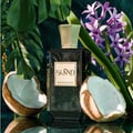 Khadlaj Island Extrait de Parfum 100ml by Khadlaj — A dark textured bottle of Khadlaj Island perfume is centered between two halves of a coconut, with tropical leaves and purple hyacinths in the background. | Khadlaj Island Extrait de Parfum 100ml by Khadlaj — Botol Khadlaj Island bertekstur gelap berpusat di antara