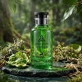 Maison Alhambra Jean Lowe Verde Aura — A green glass perfume bottle sits on a dark green marble surface, surrounded by moss, dried twigs, and sliced bergamot peels, with a blurred forest background. | Botol minyak wangi kaca hijau Maison Alhambra Jean Lowe Verde Aura terletak di atas permukaan marmar hijau gelap