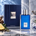 Khadlaj Karus Blu Spice by Khadlaj 100ml EDP Men — Blue ribbed bottle with silver cap, next to its matching blue textured box, with lemon slice, peppercorns, and cardamom pods on a marble surface.