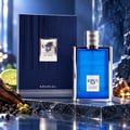 Khadlaj Karus Blu Spice — Blue glass perfume bottle with silver cap, next to its navy blue textured box, with black peppercorns, cardamom pods, wood, and a lime slice on a reflective surface.
