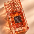 Lattafa Khamrah Mira — Amber-toned glass perfume bottle with intricate geometric patterns, set against a soft, draped fabric background with a lit candle, cinnamon sticks, chocolate chunks, and red berries.