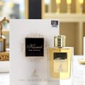 Maison Alhambra Kismet for Women 100ml — A white box with gold speckles and a black square label featuring the 'Kismet for Women' logo sits next to a clear glass perfume bottle with a gold cap and a gold label. | Maison Alhambra Kismet for Women 100ml — Kotak putih dengan bintik emas dan label segi empat hitam yang