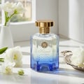 Maison Alhambra Kismet Lunar Magic 100ml by Maison Alhambra — A faceted glass perfume bottle with a gold cap and blue gradient base, surrounded by white flowers and a decorative silver tray on a white surface. | Maison Alhambra Kismet Lunar Magic 100ml by Maison Alhambra — Botol minyak wangi kaca berfaset dengan