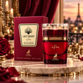 Maison Alhambra Last Night in Paris — Red glass perfume bottle and matching box on a marble surface, with a blurred Parisian cityscape and red roses in the background.