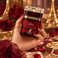 Maison Alhambra Last Night in Paris by Maison Alhambra 100ml Unisex — A hand holds a red glass perfume bottle with a gold cap and label, against a backdrop of red roses and the Eiffel Tower.