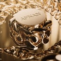 Afnan Lynked Forever by Afnan 100ml Eau De Parfum — Tampilan dekat penutup botol minyak wangi emas dengan tulisan 'AFNAN', dikelilingi rantai emas berukir dan permukaan reflektif.