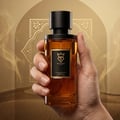 Bujairami Mad Love 100ml Extrait Unisex — Hand holding a clear glass perfume bottle with amber liquid, black cap, and a black label featuring a gold crown logo and text.