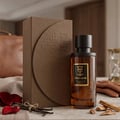 Bujairami Mad Love 100ml Extrait Unisex — Brown textured box and amber glass perfume bottle with black cap, on a marble surface with vanilla beans, rose petals, and wood chips.