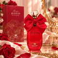 TADangel Magic Blossom — Red perfume bottle with a large red bow and crystal cap, next to its red floral box, on a silk cloth with red roses.