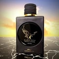 Lattafa Malik Al Tayoor Concentrated — Black square perfume bottle with a gold eagle emblem on a black marble surface, against a sunset sky background. | Botol minyak wangi hitam segi empat dengan lambang helang emas di atas permukaan marmar hitam, berlatarkan langit matahari terbenam.